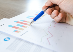 Photo of a hand with a pen on some papers with graphs